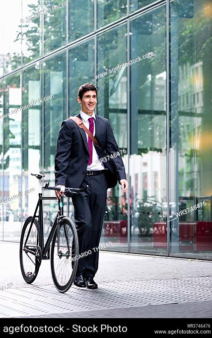 Businessman wheeling a bicycle through town along a pedestrian walkway as he commutes to work using eco-friendly transport