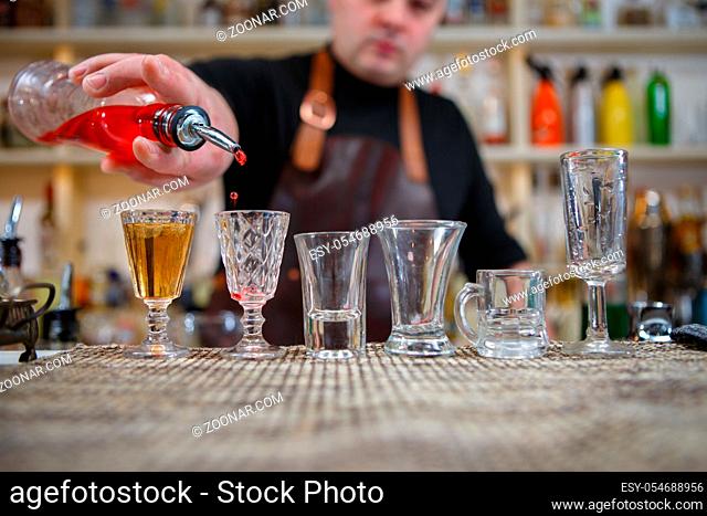 Bartender pours various of alcohol drink into small glasses on bar