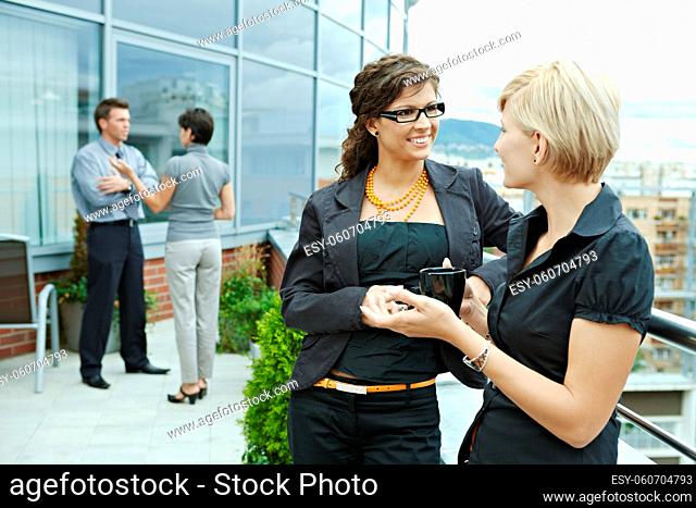 Businesswomen having break on office terrace outdoor drinking coffee talking