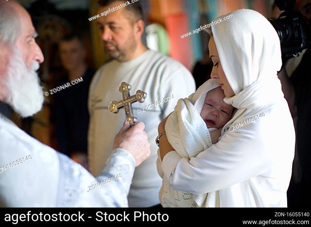 Belarus, Gomel, January 19, 2019. Prudkovsky church. Baptism of the child. Godmother with a baby and priest with a cross. Acceptance of faith