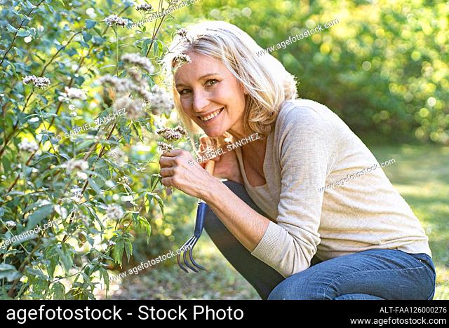 Portrait of smiling mature woman smelling flowers in backyard