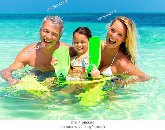 Portrait of smiling family of three in sea water with fins