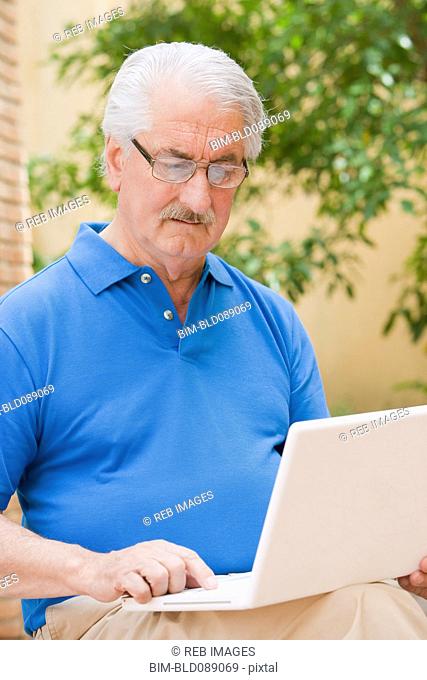 Senior Hispanic man using laptop outdoors