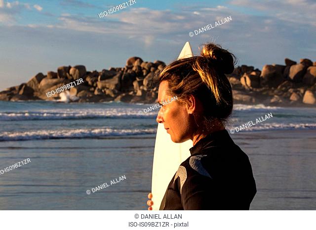 Female surfer carrying surfboard on beach, head and shoulder side view, Cape Town, Western Cape, South Africa