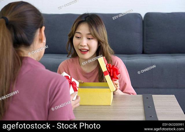 Two Asian women enjoy opening a gift box received for a special occasion. Party, people and new year holidays concept