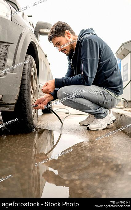 Man filling air in tire at gas station