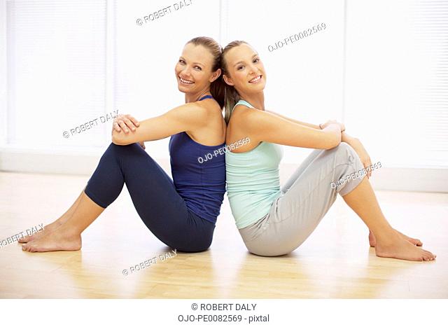 Portrait of smiling women sitting back to back in fitness studio