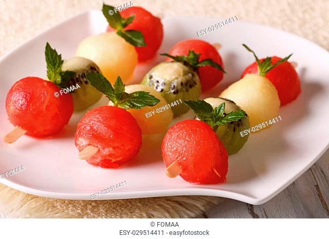 Delicious dessert: balls of watermelon, kiwi and melon on skewers close-up on a plate. horizontal