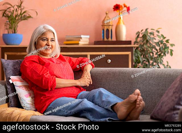 Old woman relaxing on sofa in living room