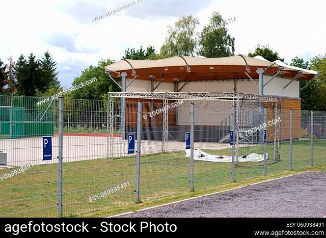 Die Veranstaltungsbühne eines Sportparks hinter einem Zaun mit Parkplätzen für Schiedsrichter und Presse