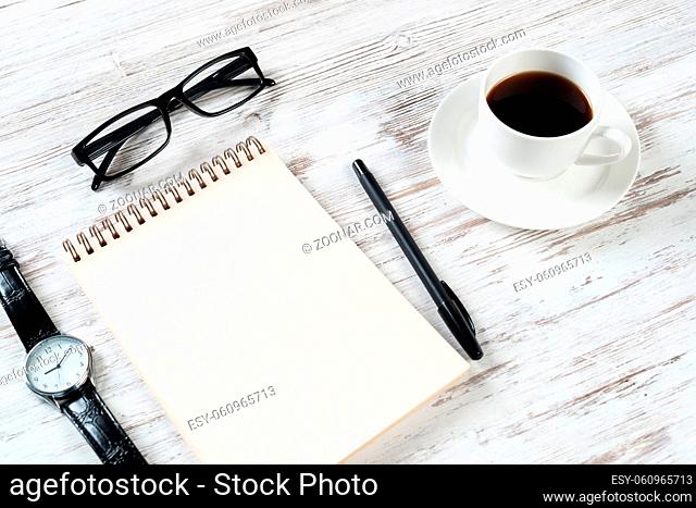 Still life of office workspace composition with cup of coffee. Flat lay grunge wooden desk with open spiral notebook, glasses and pen