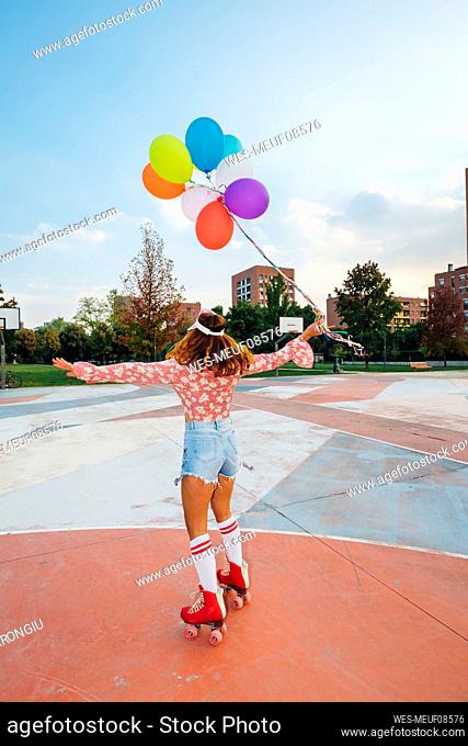 Woman with arms outstretched holding balloons roller skating at sports court