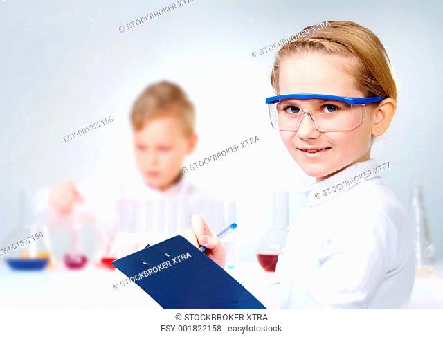 A little girl in protective glasses making notes and looking at camera