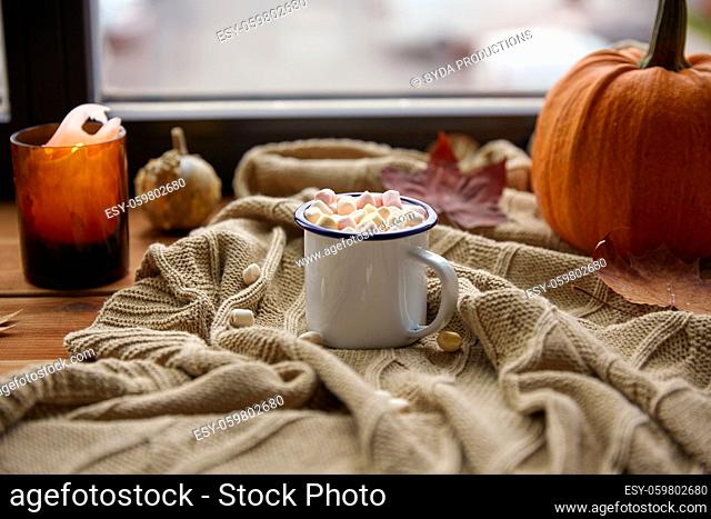 cup of marshmallow, candle and pumpkin on window