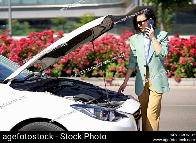 Female professional talking on smart phone while standing near broken down car
