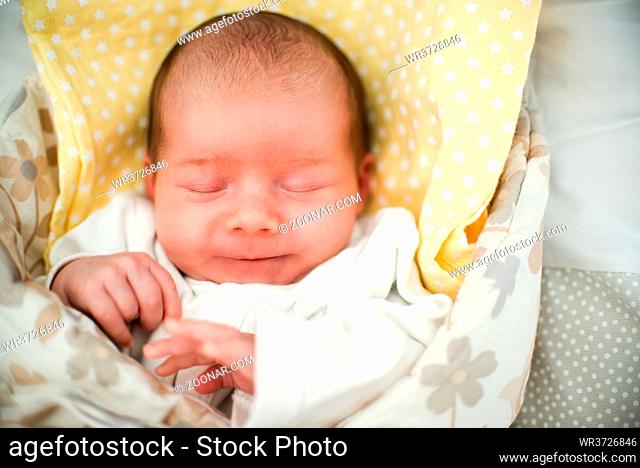 Cute newborn baby sleeping in swaddle wrap with smile on her face. Newborn theme