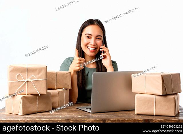 Small business owners, startup and e-commerce concept. Smiling asian woman manage online store, businesswoman answer phone call, show thumbs-up