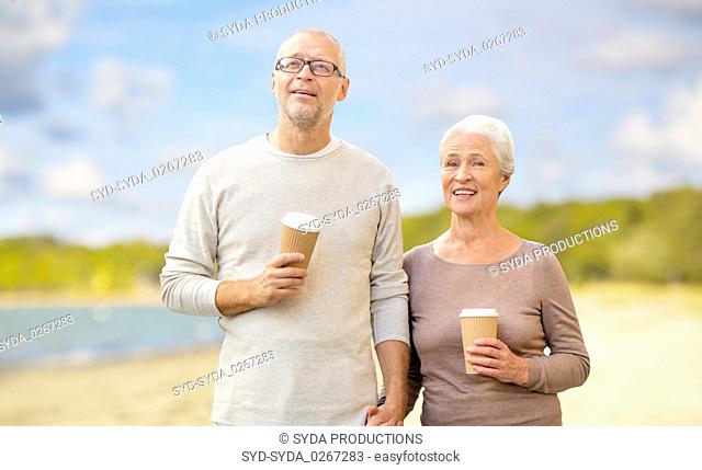 senior couple with takeaway coffee on beach
