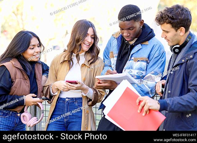 Teenager writing in book by friends at university campus