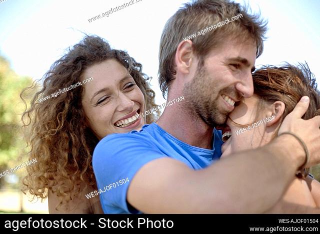 Happy curly haired woman looking at couple hugging at park