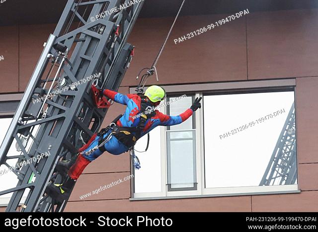 06 December 2023, Thuringia, Gera: A firefighter dressed as Spiderman abseils down from a turntable ladder and greets the children in the SRH Waldklinikum...