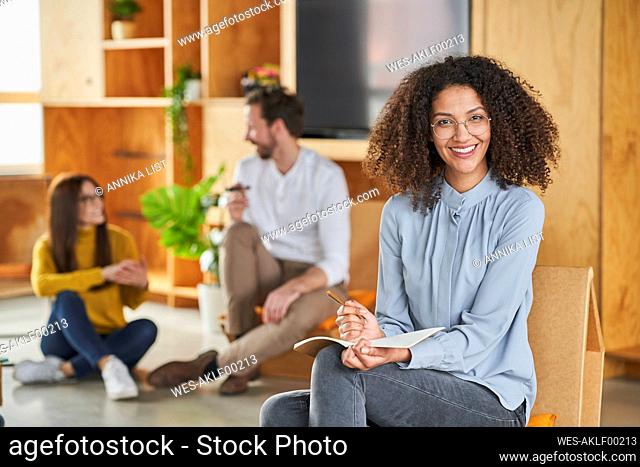 Mid adult businesswoman smiling while sitting with colleagues in background