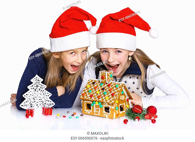 Christmas theme - Two smiling girl in Santa's hat with gingerbread house, isolated on white