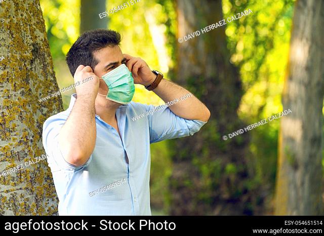 Young man standing in the park removing protective face mask celebrating victory over coronavirus outside in open air. End of quarantine. Remove mask