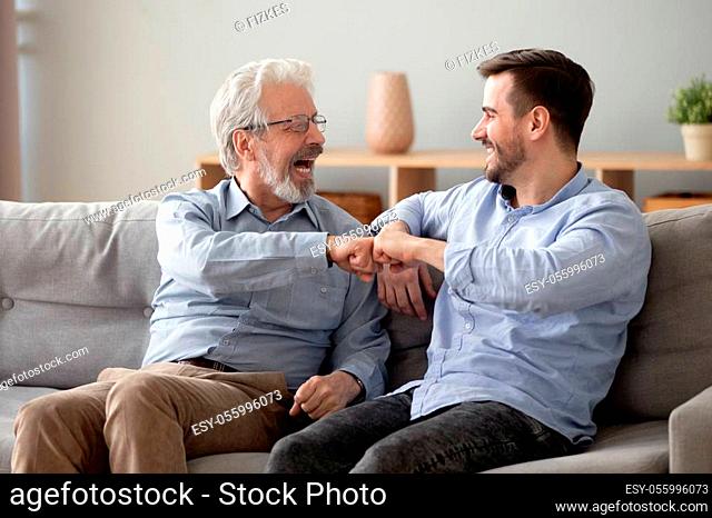 Elderly grey haired man and handsome guy giving fist bump, old father rejoices of grown up son successes congratulates him feels happy