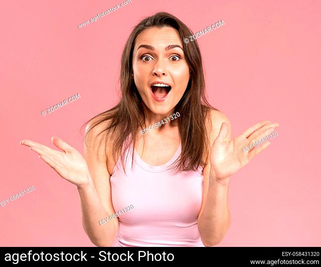 Charming acting surprised girl wearing pink t-shirt with hands in the air, excited and joy expression on her face with positive emotions