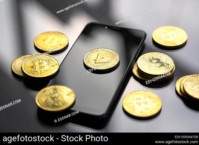 Golden litecoin coin on a smartphone with a lot of bitcoins coins on a table. Virtual cryptocurrency concept. Mining of bitcoins online bussiness