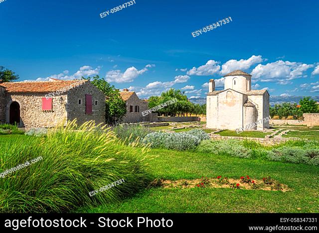 Old, dated on 9th century, Church of the Holy Cross in Nin with grass and flowers in front and mountain range of Dinaric Alps in background, Croatia