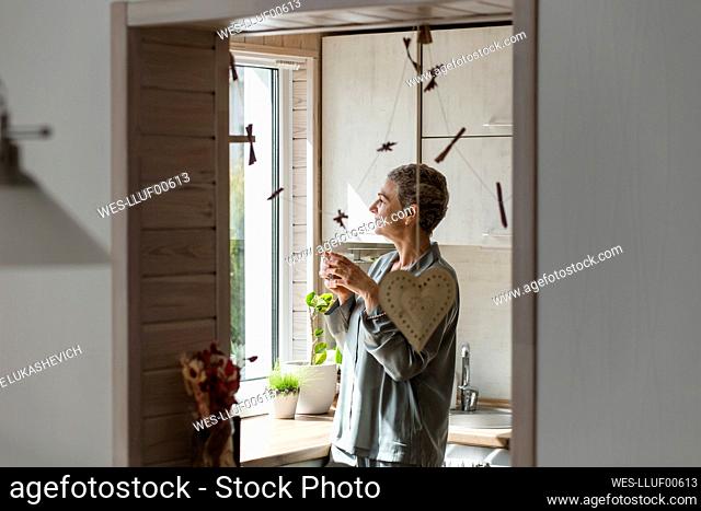 Mature woman holding tea glass in kitchen at home
