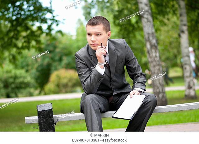 Young business man waiting for meeting, working with papers at green park. Student