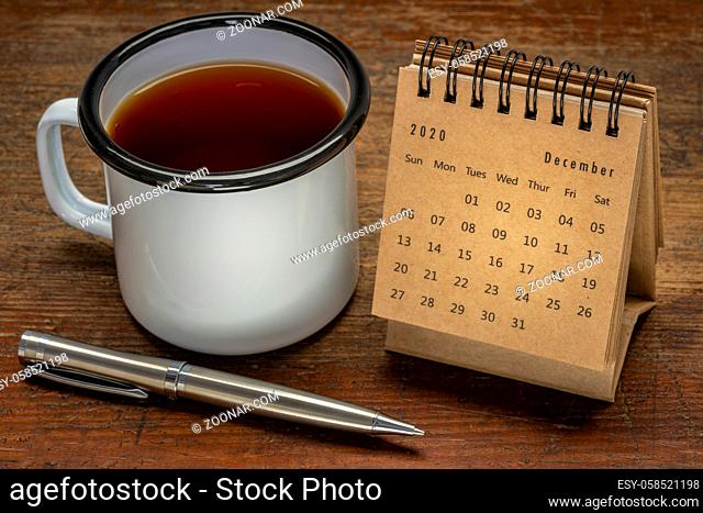 December 2020 - spiral desktop calendar on a rustic wood table with a cup of tea and pen, time and business concept