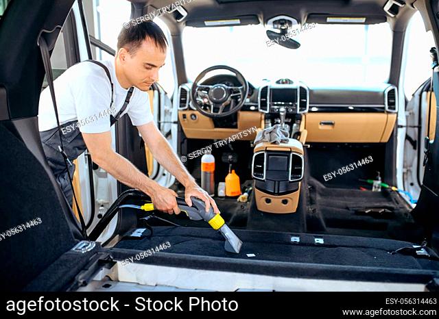 Worker cleans car interior trim with vacuum cleaner, car dry cleaning and detailing. Vehicle washing service in garage, thoroughly care of automobile