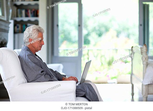 Senior man in bathrobe using laptop in bedroom