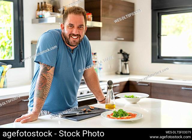 Happy mature man leaning on kitchen island at home