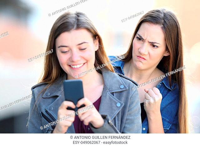 Angry girl spying the smart phone of a friend in the street