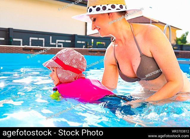 2-3 years old child with mother in swimming pool learn to swim. Baby in swimming west and red hat.Summer at home concept