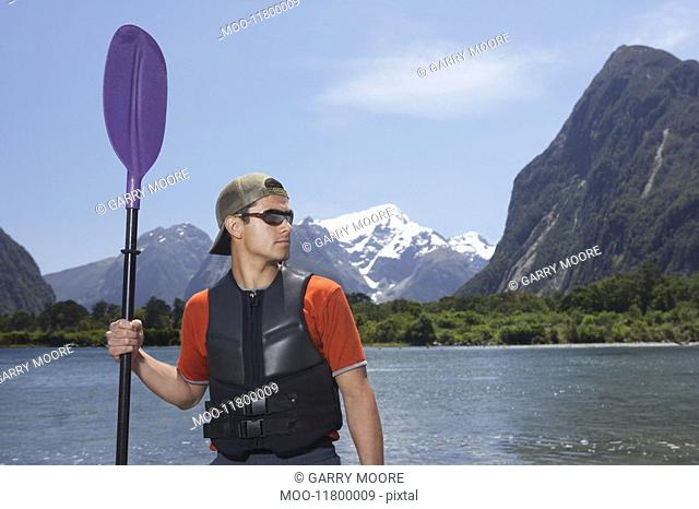 Man holding oar on shore of mountain lake