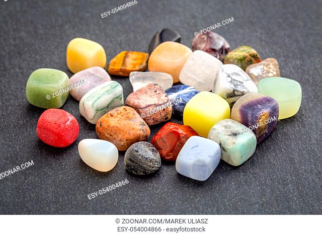 a pile of polished, semiprecious, colorful gemstones against gray slate stone