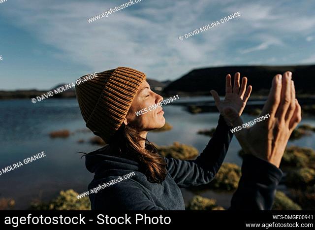Smiling woman with eyes closed gesturing at lake