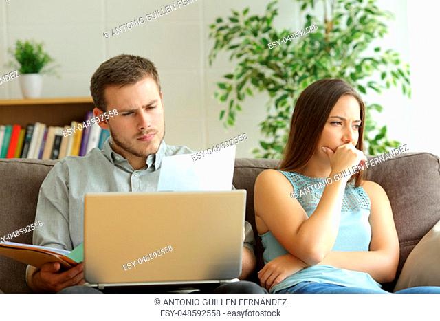 Husband addicted to work and unsatisfied wife beside him looking away sitting on a couch at home