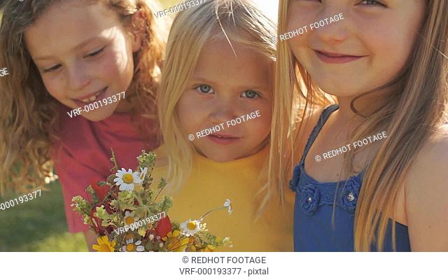 Portrait of three children with bunch of wild flowers in park