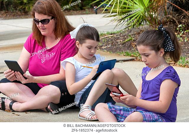 Mother and two daughters aged 6 and 8 playing and learning in front of home relaxing with games and computers learning