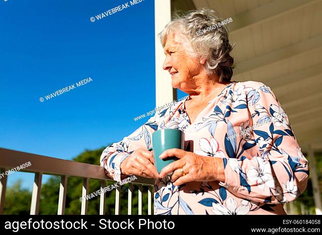 Senior caucasian woman standing on balcony holding mug and smiling