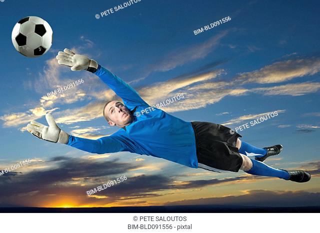 Caucasian soccer goalie jumping in mid-air catching ball
