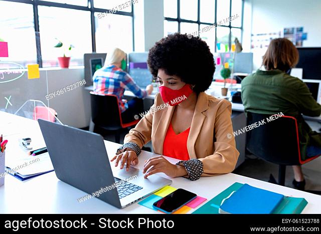 Mixed race businesswoman wearing face mask in creative office