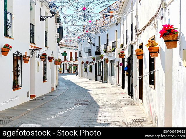 Mijas white washed street, small famous village in Spain. Charming empty narrow streets with New Year decorations, on houses walls hanging flower pots